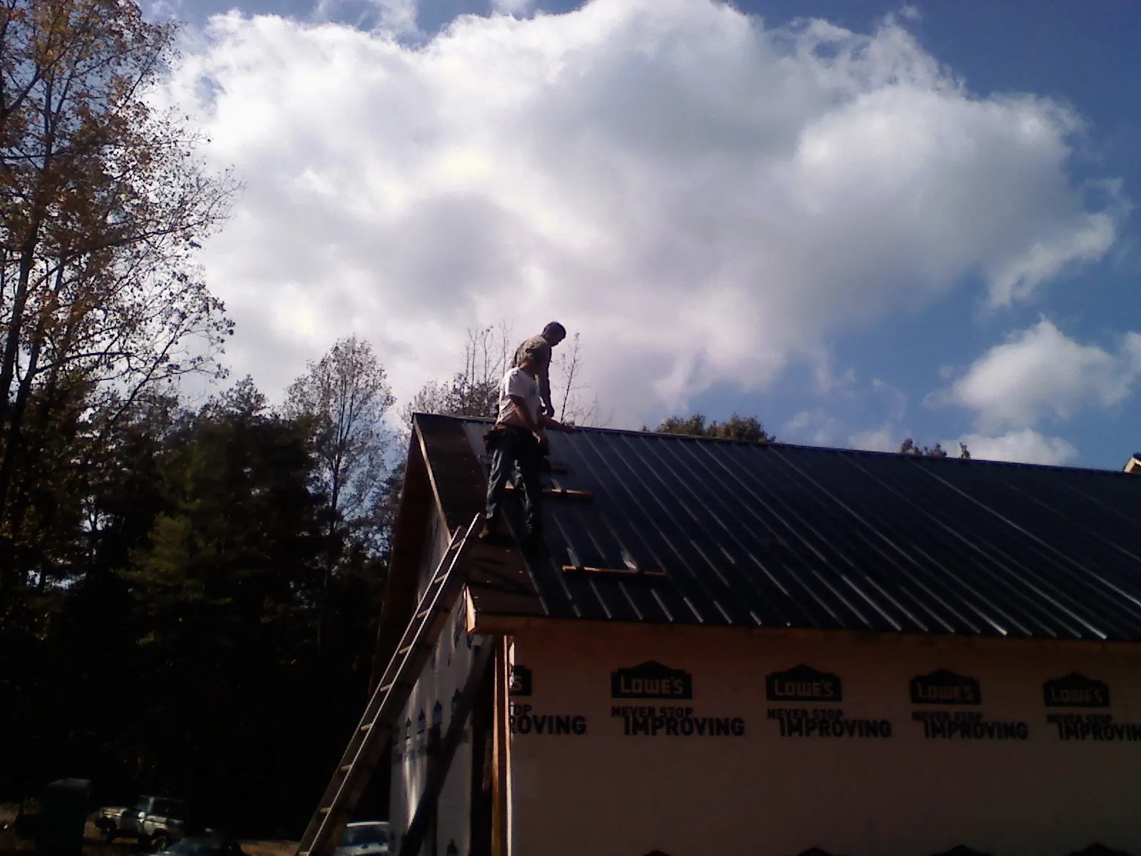 Roofer fastening dark metal panels high against a cloudy sky, from a Roof Inspection job in Euclid