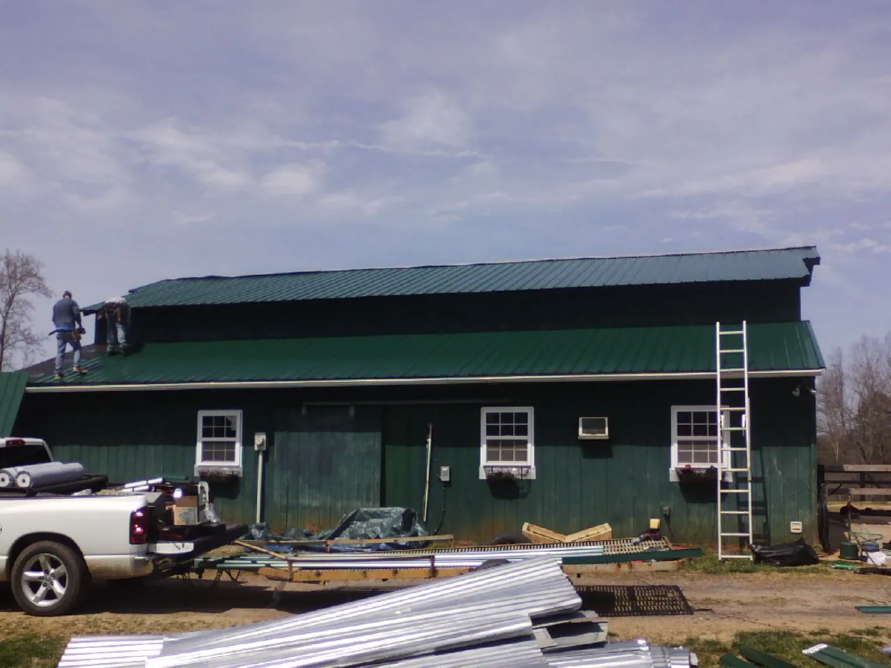 Crew installing green metal roofing on a large green barn in Euclid
