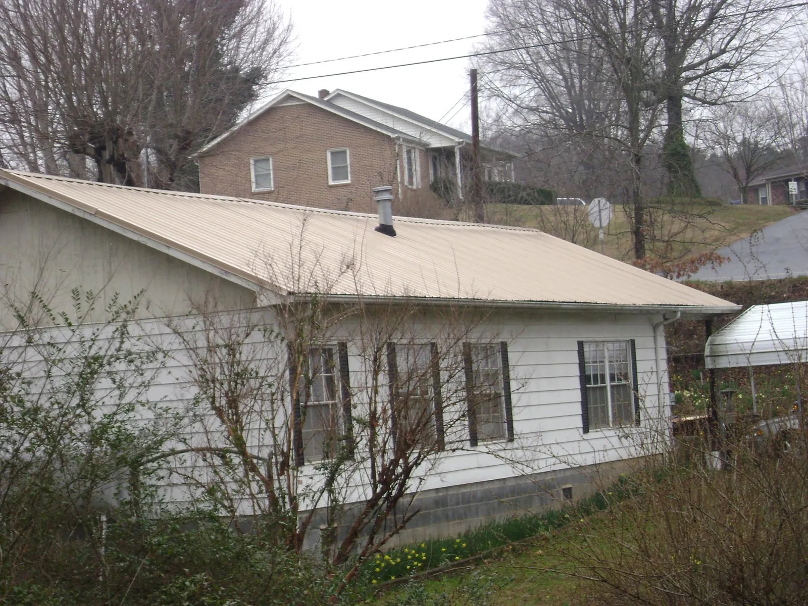 Tan metal roof on a white sided house set into a hillside — Commercial Roofing by Roofing Brothers in Euclid